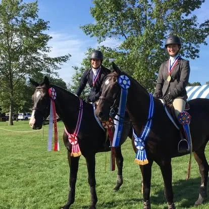 Two mounted riders with horses draped in multiple championship ribbons