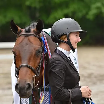 Smiling rider in helmet beside bay horse with ribbons