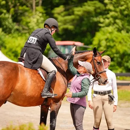 Trainer coaches a mounted rider in a hunter jacket beside a bay horse